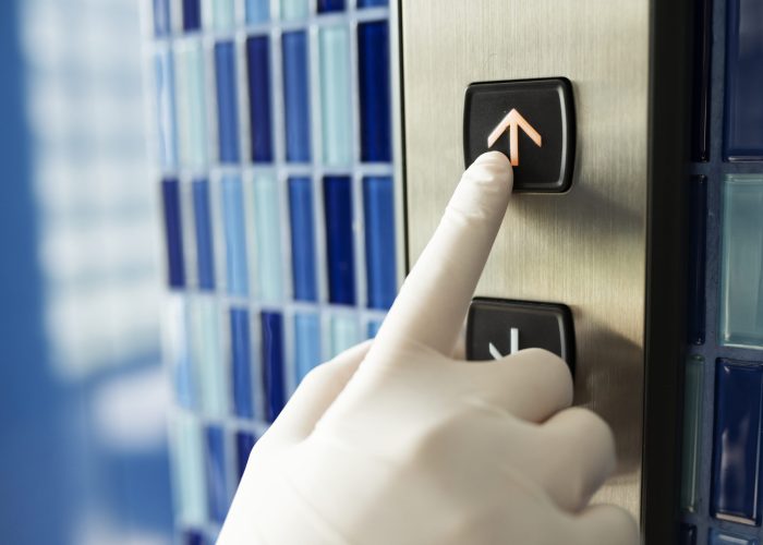 Gloved hand pressing an elevator button to prevent coronavirus contamination